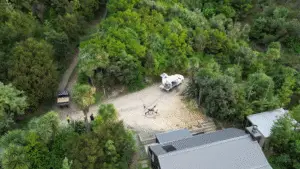 Aerial view of a drone spray trailer and agricultural drone operating in a forested rural property.