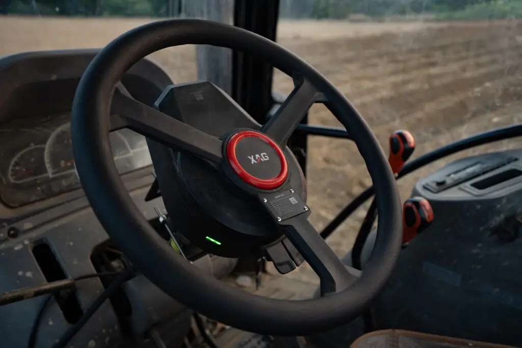 Close-up of the XAG APC2 AutoPilot Console automated steering wheel inside a tractor cab, showing the integrated control module for precision farming.