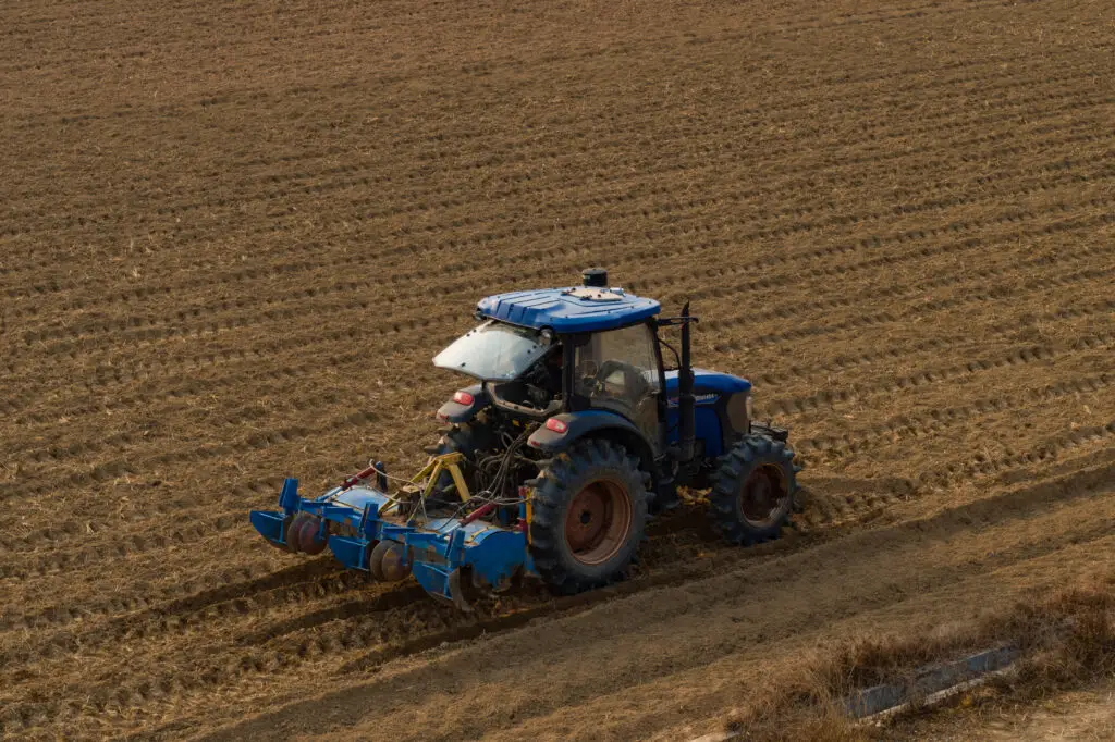 Blue tractor equipped with an APC2 AutoPilot Console system ridging soil in a large farmland field.